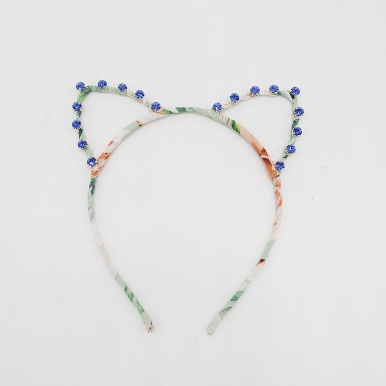 May include: A floral patterned headband with blue rhinestone accents in the shape of cat ears.