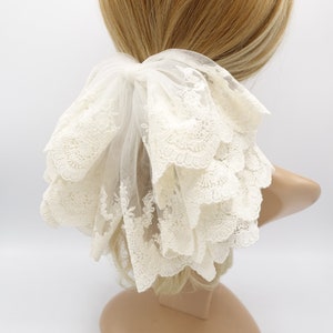 May include: White lace hair scrunchie with a ruffled design. The scrunchie is made of delicate lace and has a soft, feminine look.