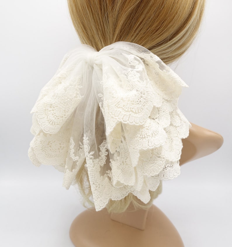 May include: White lace hair scrunchie with a ruffled design. The scrunchie is made of delicate lace and has a soft, feminine look.