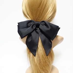 Peut inclure: Un grand nœud en satin noir pour cheveux. Le nœud est noué en un grand nœud plein et est sécurisé par un petit élastique.