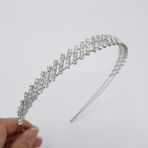 Puede incluir: Una diadema plateada con un diseño en zigzag adornado con brillantes pedrería transparente. La diadema, fina y delicada, es adecuada para ocasiones especiales o para añadir un toque de glamour a cualquier look.