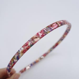 May include: A thin, floral patterned headband with a pink, white, and multi-colored design.