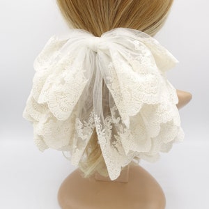 May include: White lace hair bow with a large, layered bow and a delicate floral pattern. The bow is tied with a white ribbon and is perfect for adding a touch of elegance to any hairstyle.
