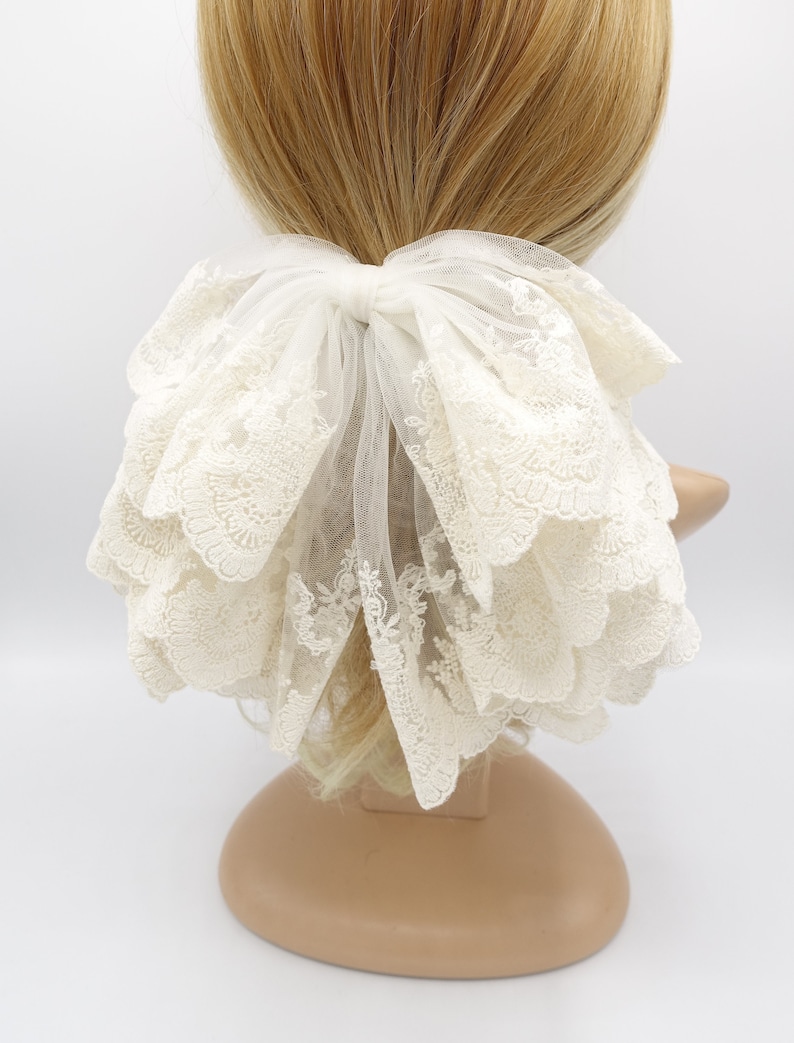May include: White lace hair bow with a large, layered bow and a delicate floral pattern. The bow is tied with a white ribbon and is perfect for adding a touch of elegance to any hairstyle.