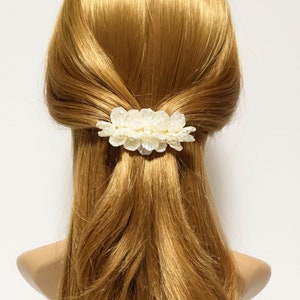 May include: A white flower hair clip with a pearl-like finish. The clip is made of fabric and has a delicate, feminine design.