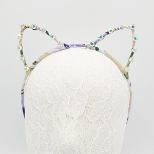May include: A headband with a floral pattern and rhinestones in the shape of cat ears.