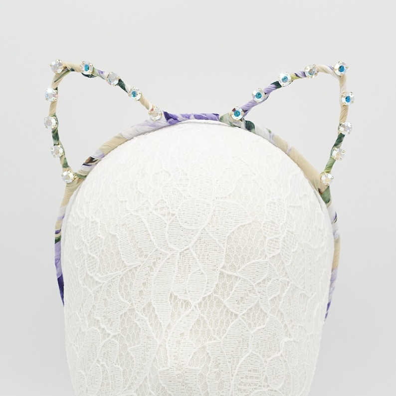 May include: A headband with a floral pattern and rhinestones in the shape of cat ears.