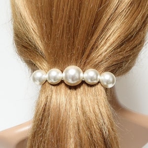 May include: A white pearl hair clip with five large pearls. The pearls are arranged in a row and are attached to a metal bar.