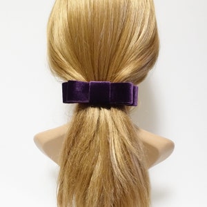 May include: A purple velvet bow hair clip. The bow is tied in a simple knot and is attached to a clip.