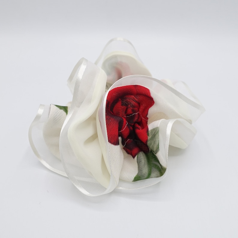 May include: White hair scrunchie with a red rose print. The scrunchie is made of a soft, sheer fabric with a white satin ribbon trim.