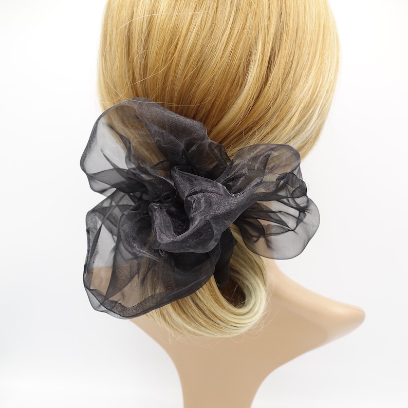 May include: Black sheer fabric hair scrunchie. The scrunchie is tied in a large bow shape.