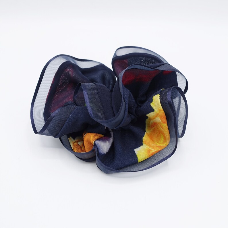 May include: A navy blue hair scrunchie with a floral print featuring yellow, red, and white roses. The scrunchie is made of a soft, sheer fabric.