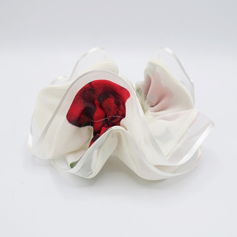May include: White hair scrunchie with a red rose print. The scrunchie is made of a soft, silky fabric and has a gathered, ruffled design.