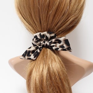 May include: A brown and black leopard print hair tie with a bow. The hair tie is tied around a ponytail of long, light brown hair.