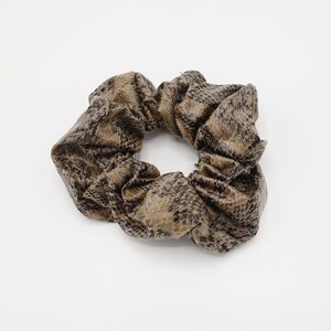 May include: A brown and tan scrunchie with a snakeskin pattern. The hair accessory is made of a soft, gathered fabric and is designed to hold hair in place. The scrunchie is a stylish hair accessory.