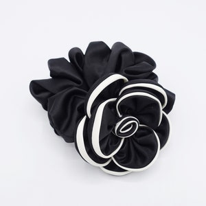 May include: Black satin hair scrunchie with a white trim, shaped like a flower.