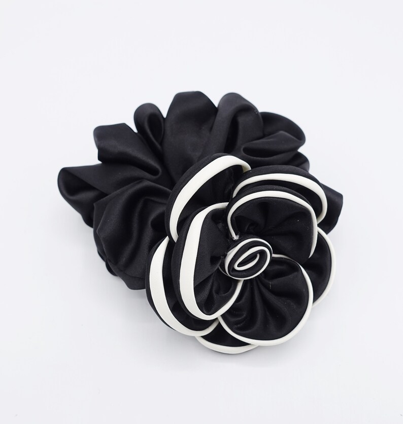 May include: Black satin hair scrunchie with a white trim, shaped like a flower.
