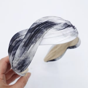 Puede incluir: Una diadema de color blanco y gris con estampado tie-dye y diseño de nudo retorcido.