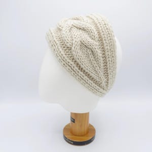 Puede incluir: Diadema de punto trenzado color crema, exhibida en una cabeza de maniquí blanca. La diadema presenta un diseño de punto trenzado grueso y texturizado y detalles acanalados. El color neutro lo convierte en un accesorio versátil. La diadema mide aproximadamente 10 cm de ancho.