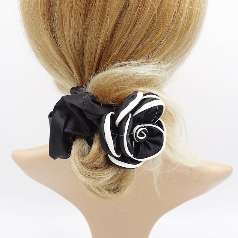 May include: Black and white satin flower hair scrunchie. The flower is made of multiple layers of fabric and has a white outline.