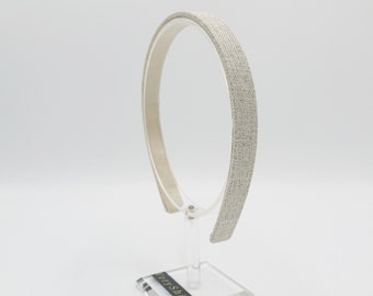 May include: A neutral-coloured headband with a textured fabric surface, displayed on a clear acrylic stand. The headband is a simple, elegant design, suitable for various hairstyles. The stand has a rectangular base with the text "veryShine".