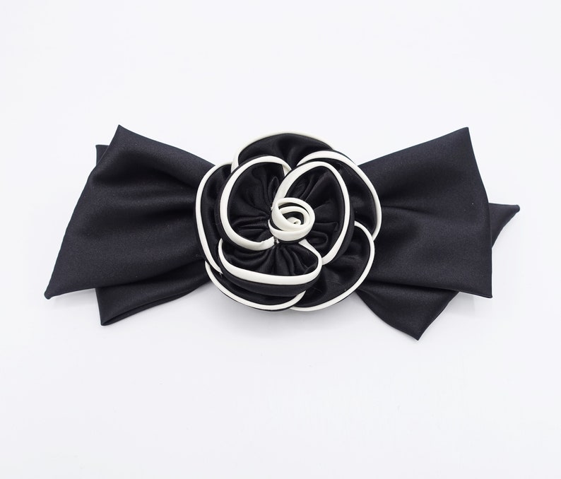 May include: A black satin bow with a large white and black fabric rose in the center.