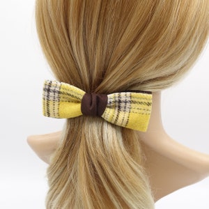 May include: A yellow and brown plaid bow hair clip. The bow is tied in a classic shape and has a brown centre.
