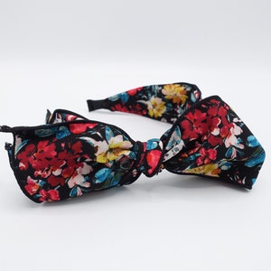 May include: A black headband with a large floral bow. The bow is made of a black fabric with a colorful floral print. The headband is a great accessory for adding a touch of style to any outfit.