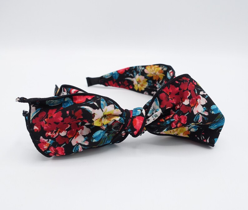 May include: A black headband with a large floral bow. The bow is made of a black fabric with a colorful floral print. The headband is a great accessory for adding a touch of style to any outfit.