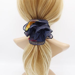 May include: A navy blue and floral patterned hair scrunchie. The scrunchie is made of a soft, silky fabric and is tied in a knot.