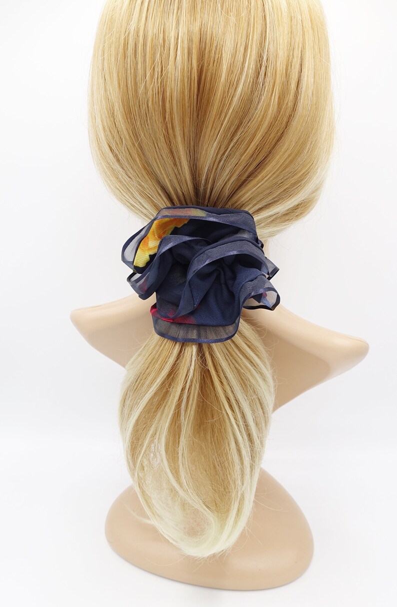 May include: A navy blue and floral patterned hair scrunchie. The scrunchie is made of a soft, silky fabric and is tied in a knot.