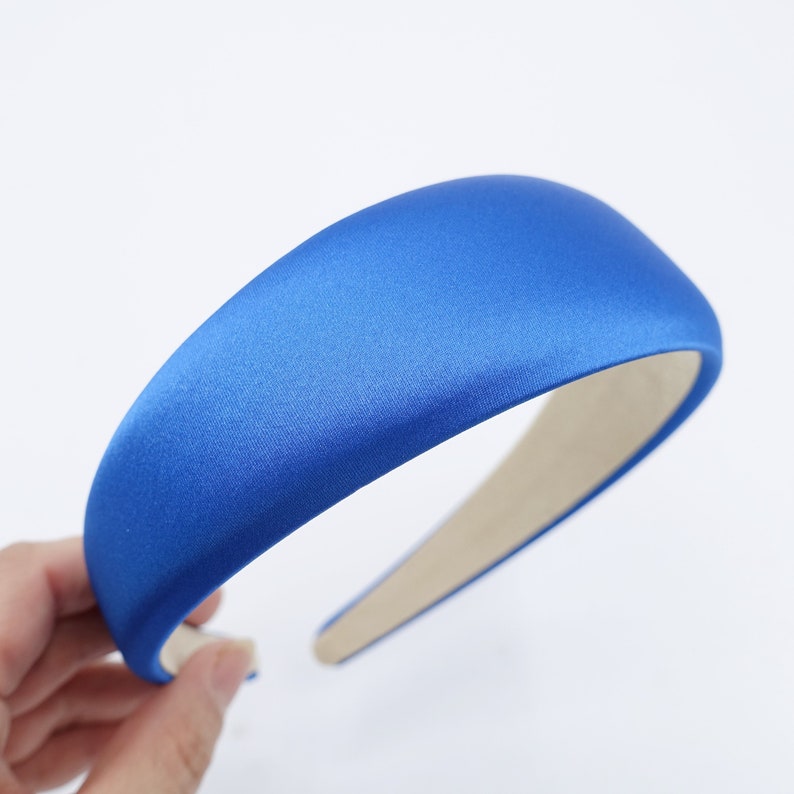 May include: A royal blue satin headband with a padded, rounded top. The interior of the headband is a light beige color. The headband is a hair accessory.