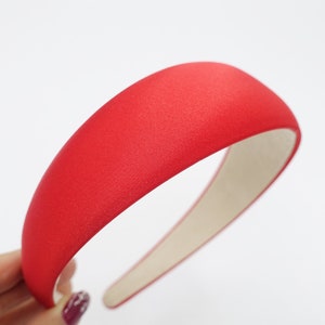 May include: A vibrant red headband with a wide, padded design. The headband is covered in a textured fabric and has a neutral-colored interior. This hair accessory is a stylish addition to any outfit.