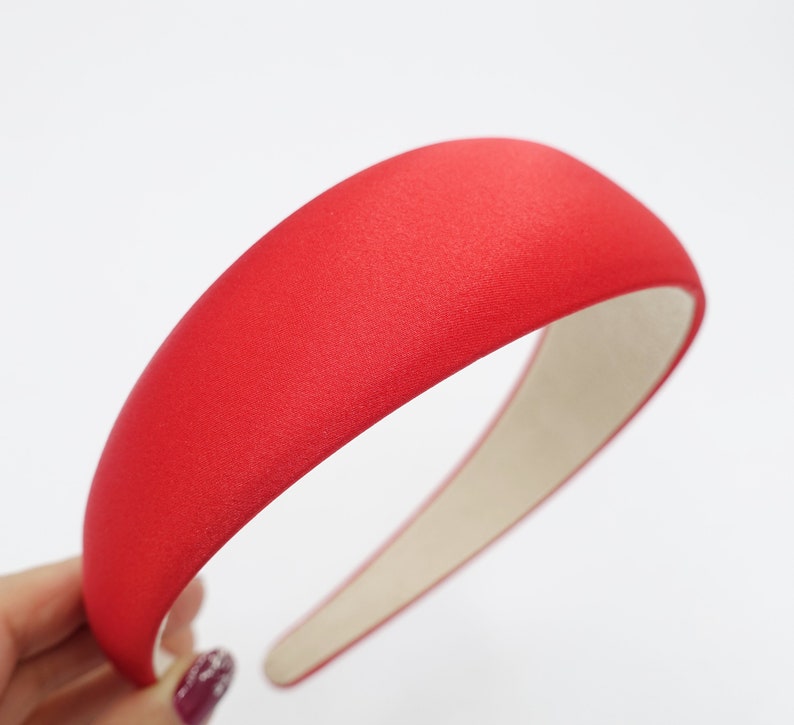 May include: A vibrant red headband with a wide, padded design. The headband is covered in a textured fabric and has a neutral-colored interior. This hair accessory is a stylish addition to any outfit.