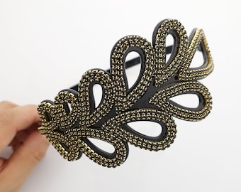 May include: Black headband with a gold leaf design. The headband is made of plastic and is decorated with small gold beads.