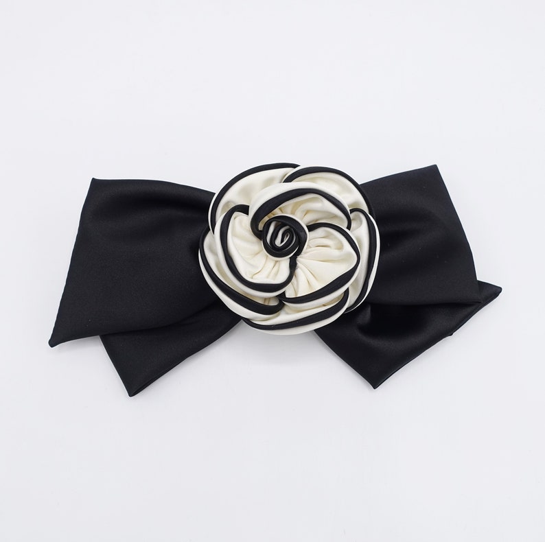 May include: A black satin bow with a white and black fabric rose in the center.
