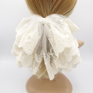 May include: A white lace hair bow with a large, layered bow and a delicate floral pattern. The bow is tied with a white ribbon and is perfect for adding a touch of elegance to any hairstyle.