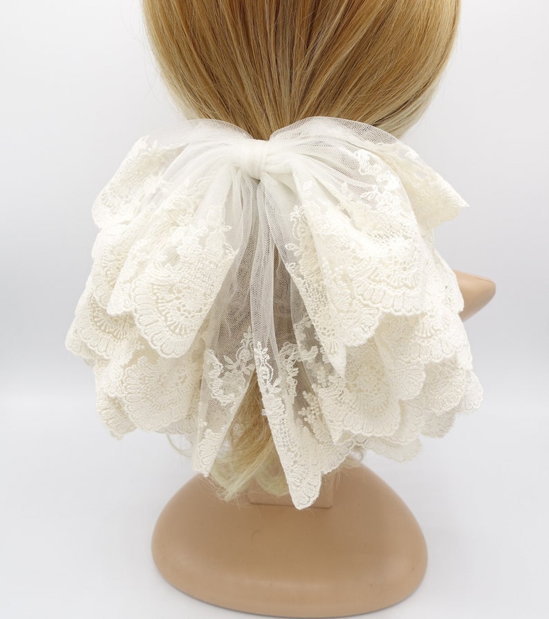 May include: A white lace hair bow with a large, layered bow and a delicate floral pattern. The bow is tied with a white ribbon and is perfect for adding a touch of elegance to any hairstyle.