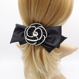 May include: A black satin hair bow with a large white and black rosette in the center. The bow is tied around a ponytail.