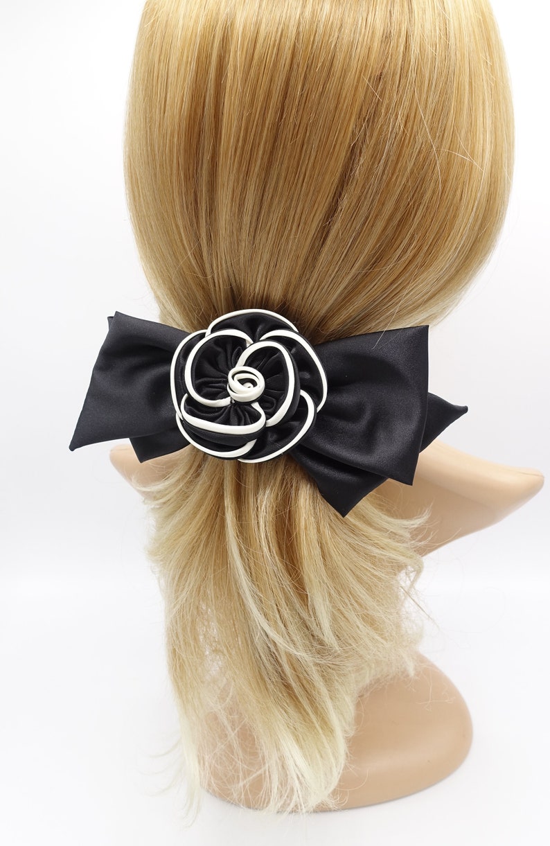 May include: A black satin hair bow with a large white and black rosette in the center. The bow is tied around a ponytail.