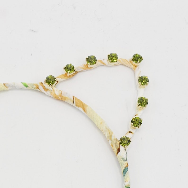 May include: A white headband with a floral pattern and green rhinestones.