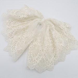 May include: A white lace trim with a delicate floral pattern. The trim is soft and flowing, with a scalloped edge.