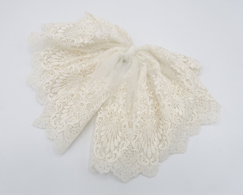 May include: A white lace trim with a delicate floral pattern. The trim is soft and flowing, with a scalloped edge.
