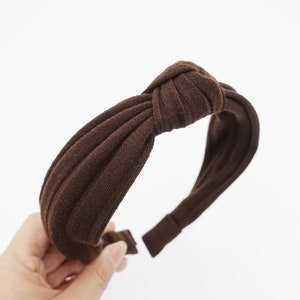 May include: A brown fabric headband with a knotted design. The headband is made of a soft, stretchy material and is perfect for adding a touch of style to any outfit.