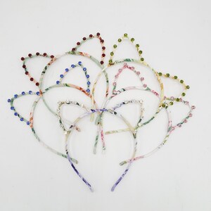 May include: A set of six colorful floral patterned headbands with jeweled cat ears. The headbands are made of fabric and have a thin metal band.