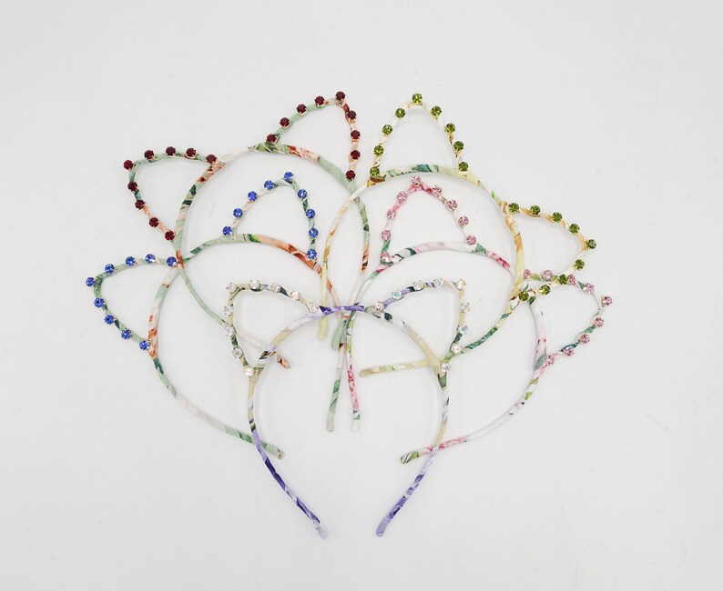 May include: A set of six colorful floral patterned headbands with jeweled cat ears. The headbands are made of fabric and have a thin metal band.