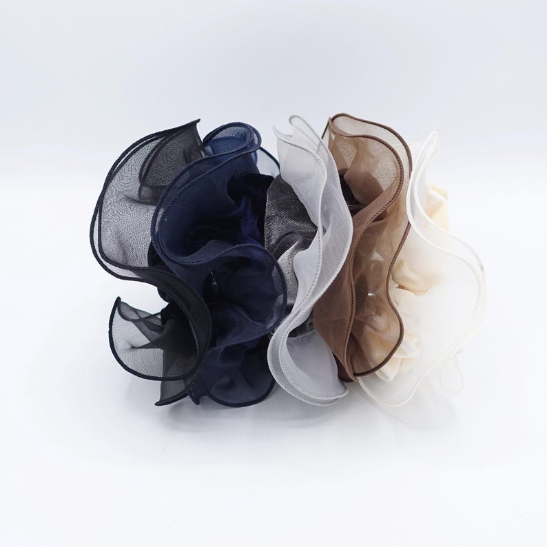 May include: A collection of ruffled fabric hair accessories in various colors. The colors include black, navy blue, gray, white, brown, and cream. The accessories are made of a sheer, lightweight material, and are bunched together.