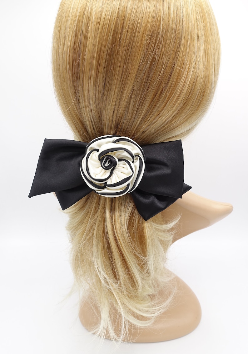 May include: A black satin bow with a white and black striped flower accent. The bow is attached to a hair clip.