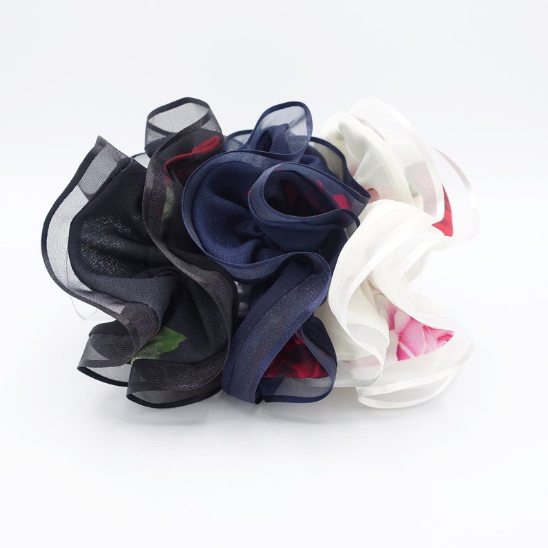 May include: Three fabric hair scrunchies in a ruffled design. One is black with a floral print, one is navy blue with a floral print, and one is white with a floral print.