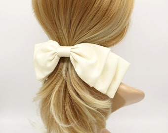 May include: A large, ivory satin bow hair clip. The bow is tied in a classic shape with a center loop and two flowing tails.
